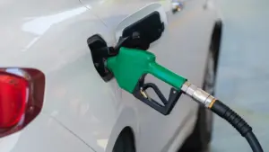Pistolet dystrybutora paliwa wlewa paliwo do baku białego samochodu osobowego.